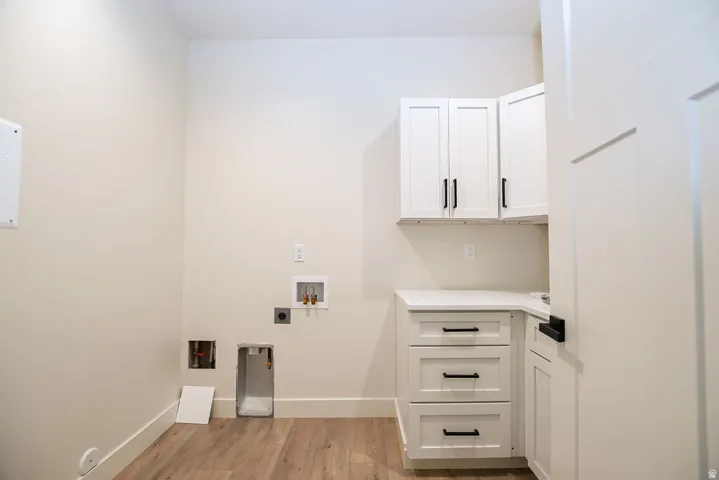 White shaker-style cabinetry with matte black hardware, light-toned wood-finish flooring, a white countertop, and a solid core door