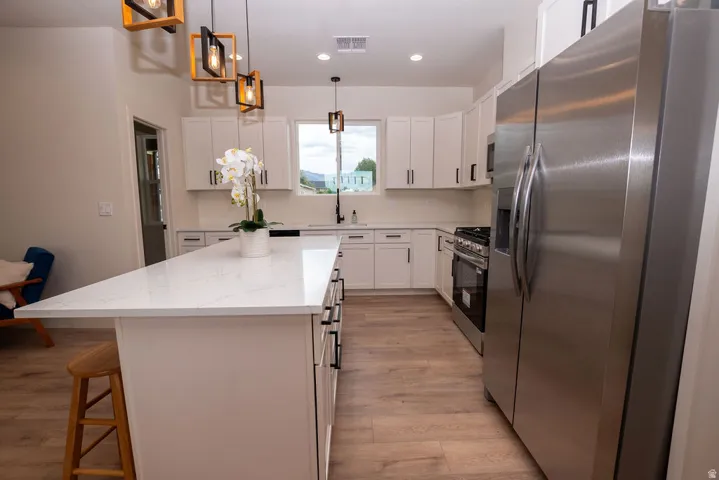 Kitchen featuring a large island with a light-toned countertop, white cabinetry with dark hardware, stainless steel appliances, and wood-finish flooring