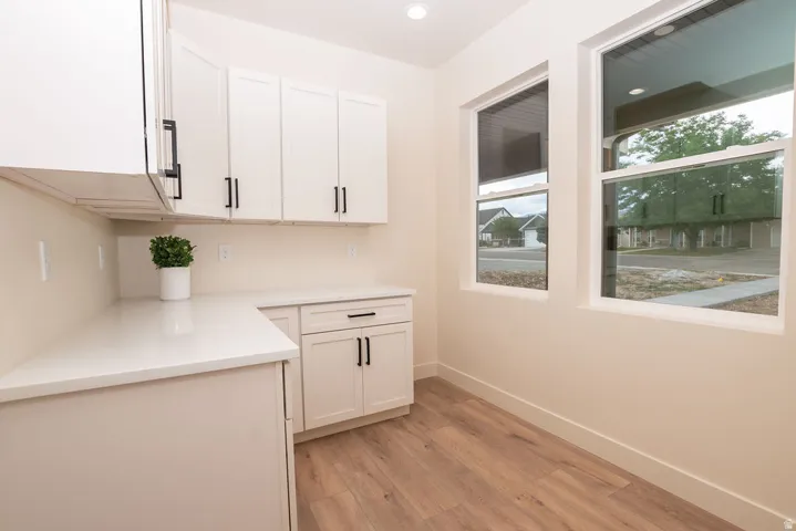 White shaker cabinetry with matte black hardware, light-toned countertops, wood-finish flooring, recessed lighting, and multiple windows