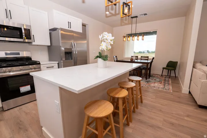 Kitchen featuring a white quartz-finish island, stainless steel appliances, white cabinetry, and wood-finish flooring
