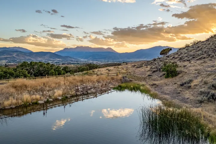 Expansive natural landscape featuring a serene water body with natural vegetation, sloped terrain, and distant mountain ranges