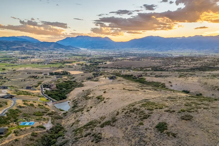 Expansive mountain scenery with distant urban areas, green valleys, and a prominent pond