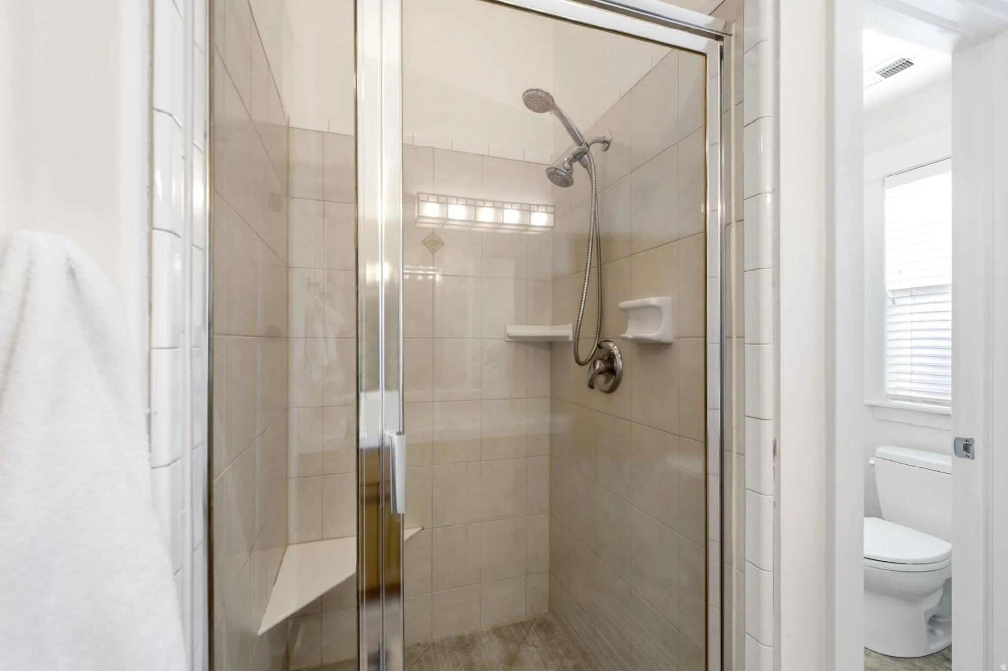 Glass-enclosed shower with a handheld showerhead, tiled walls, and a built-in bench