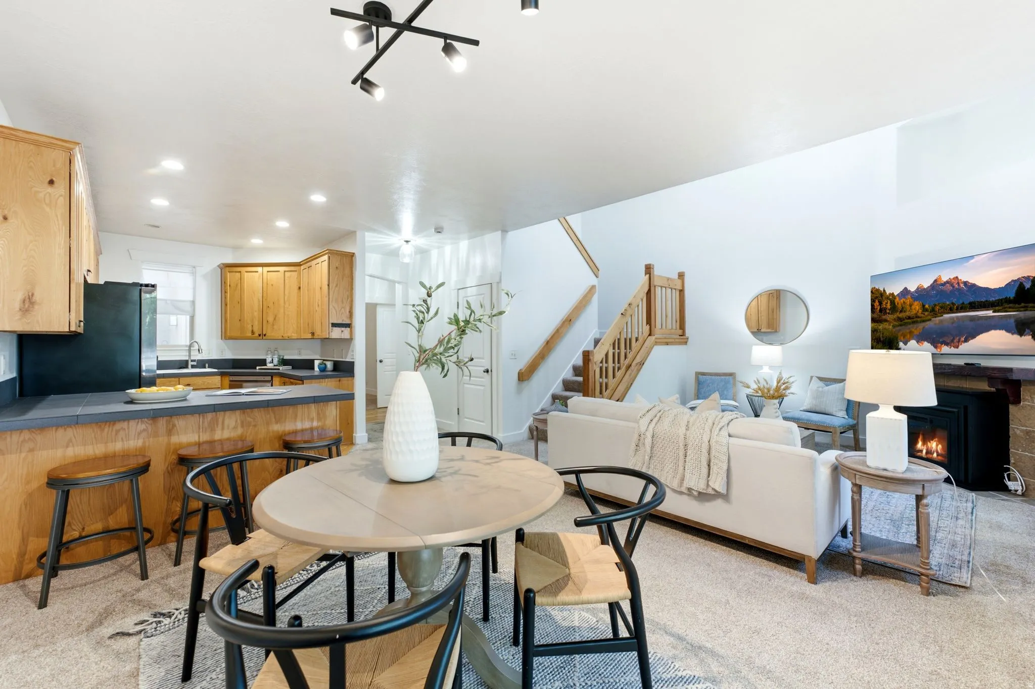 Open-concept living area with a kitchen island, wood cabinetry, built-in fireplace, and a staircase with wood railing