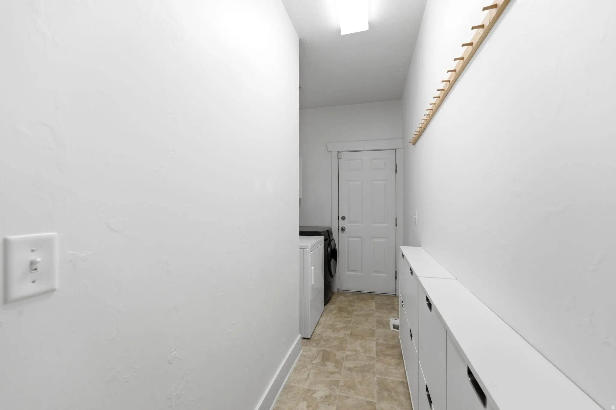 Laundry area with a neutral tone floor, overhead lighting, and built-in storage units