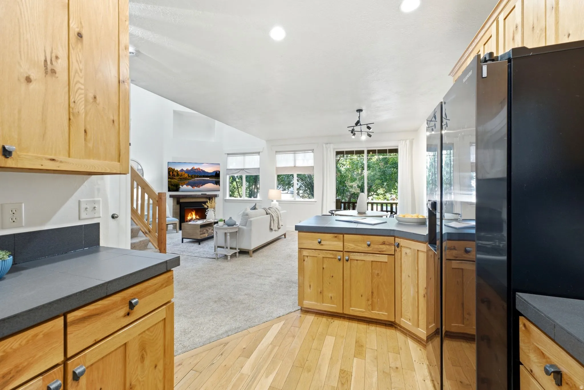 Open-concept living space featuring wood-finish flooring, a kitchen with natural wood cabinetry and dark countertops, and a living area with vaulted ceilings and a fireplace