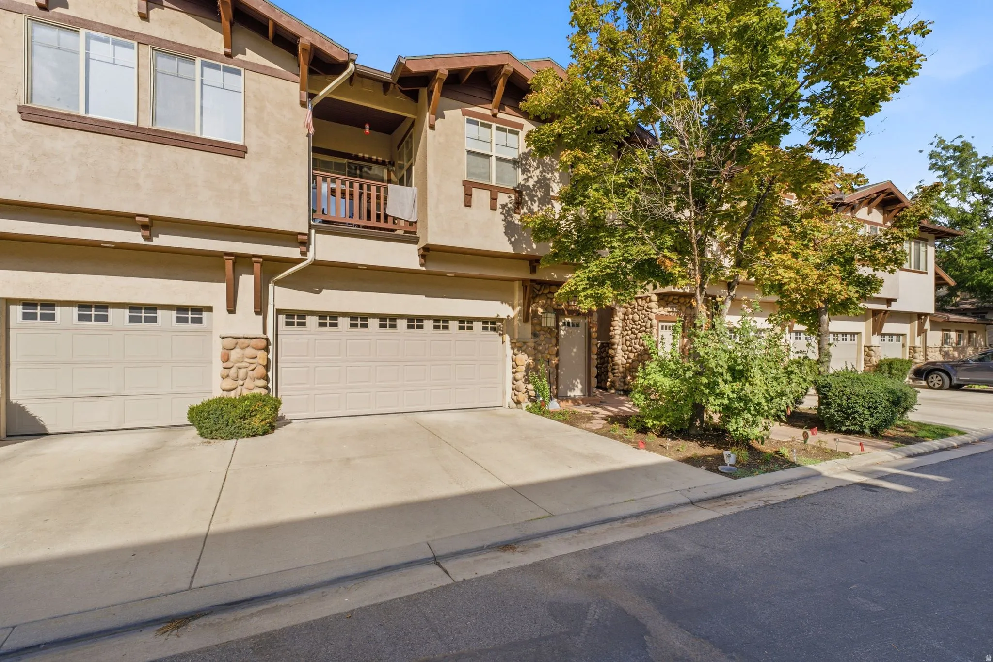 Stucco exterior with stone accents, exposed rafter tails, private balcony, and an attached two-car garage