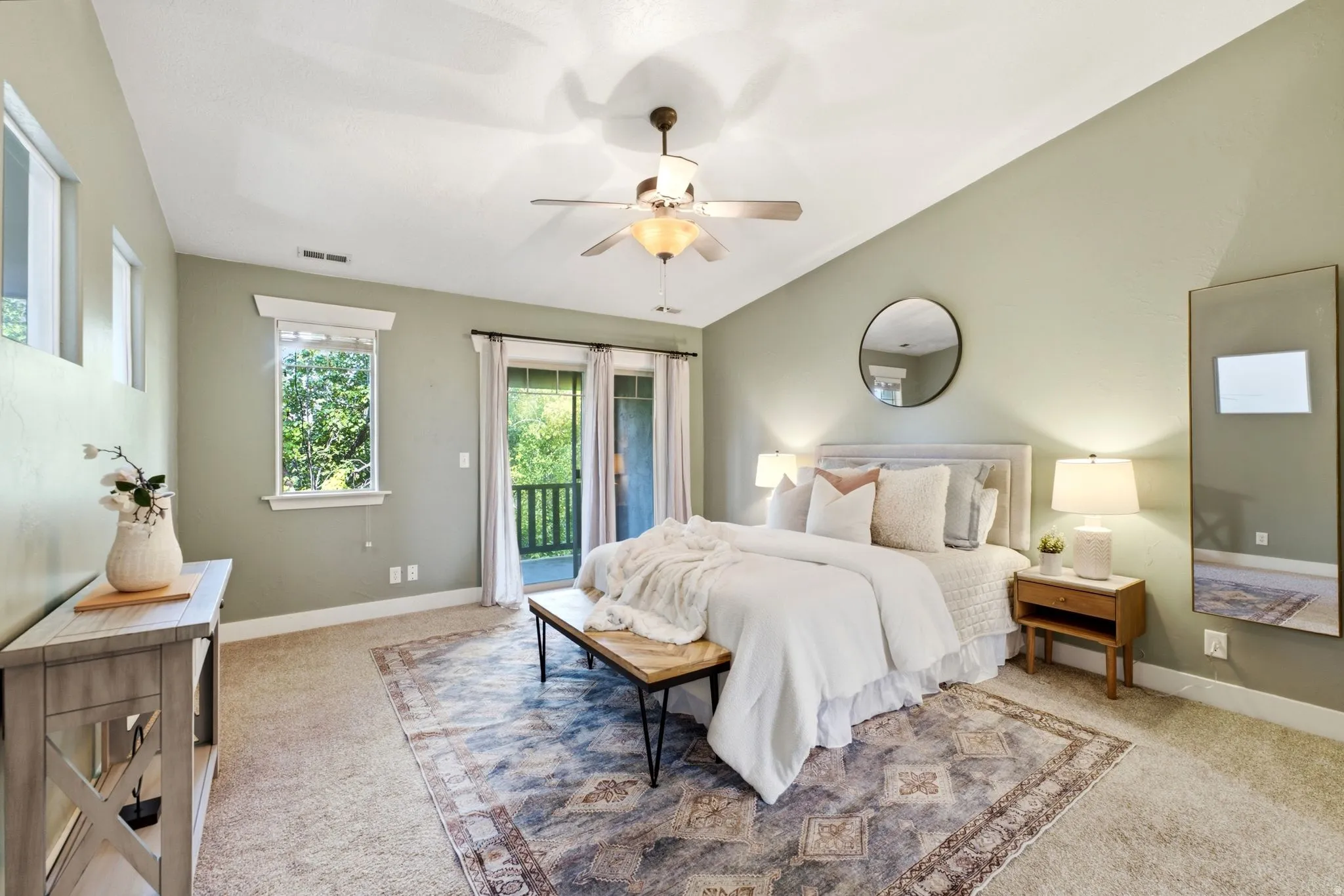 Vaulted ceiling with ceiling fan, light green wall finishes, carpet flooring, and a glass-paneled door leading to a balcony