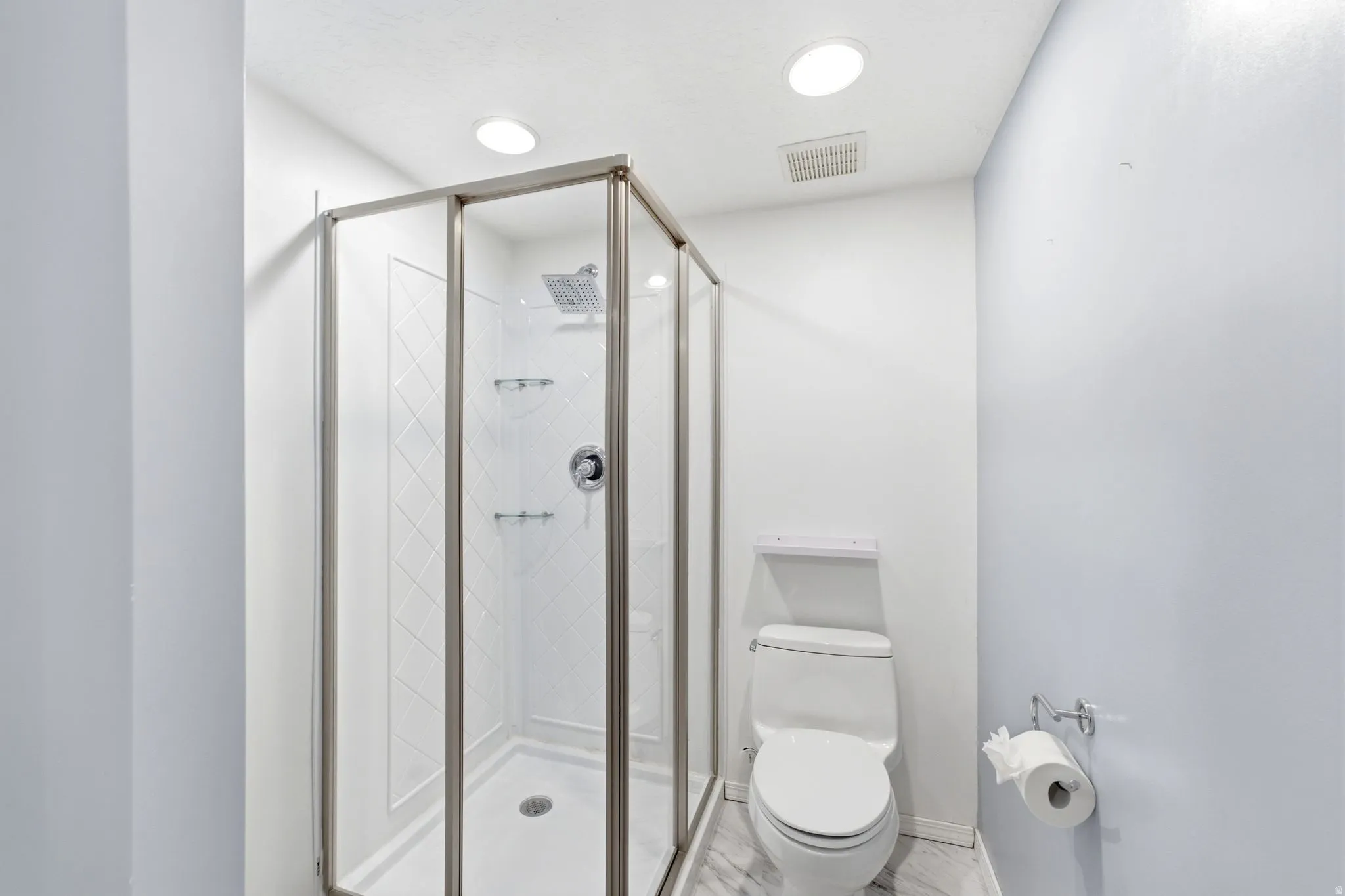 Glass-enclosed shower with a rainfall showerhead, white tile surround, and built-in shelving