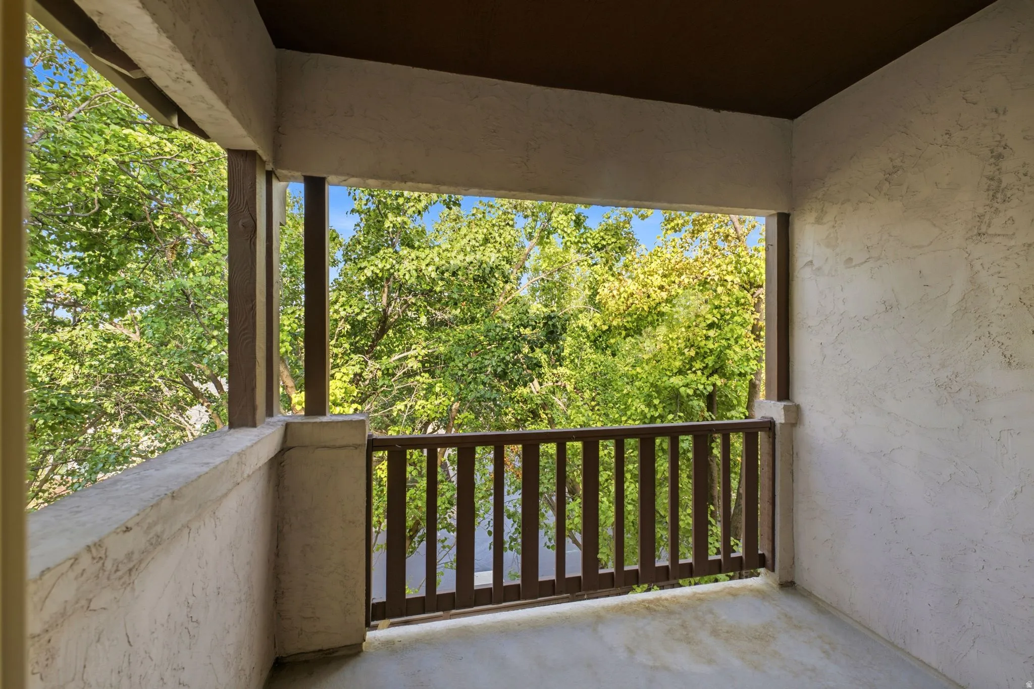 Balcony featuring a stucco exterior, wood-finish railing, and exposed ceiling beams