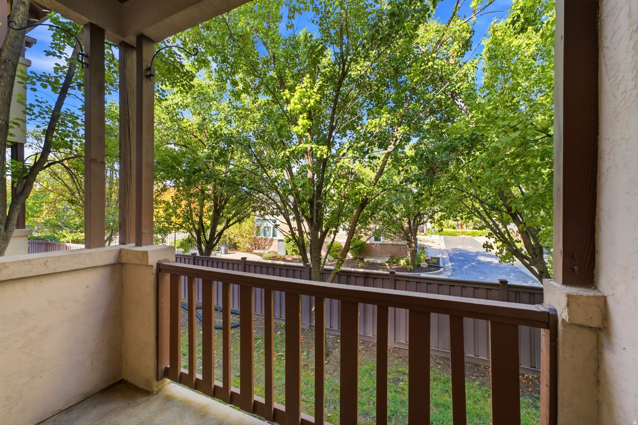 Balcony featuring wood railings, substantial support columns, and a textured stucco exterior