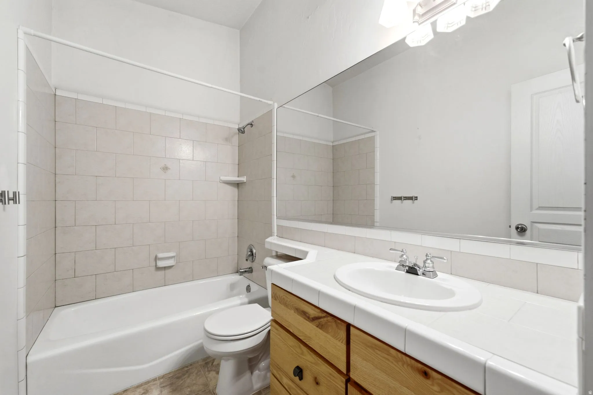Bathtub with tiled surround, wood-finish vanity with an integrated sink, and a large wall-mounted mirror