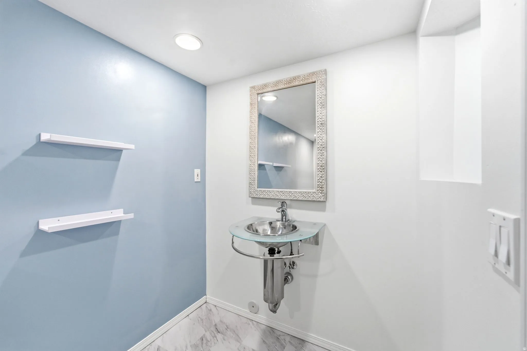 Pedestal sink with a glass basin and chrome fixtures, illuminated by a recessed ceiling light