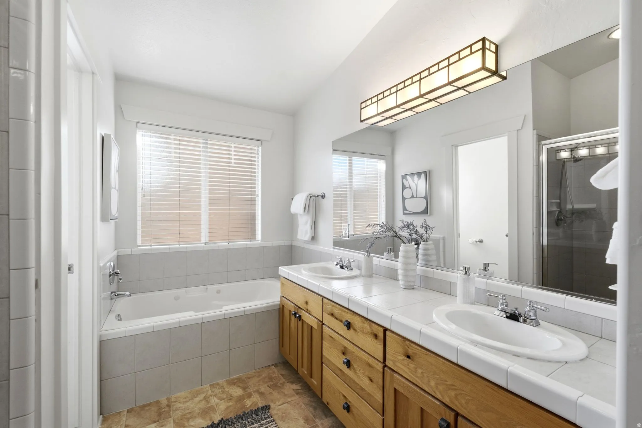 Dual vanity with wood-finish cabinetry, tile countertop, and integrated sinks