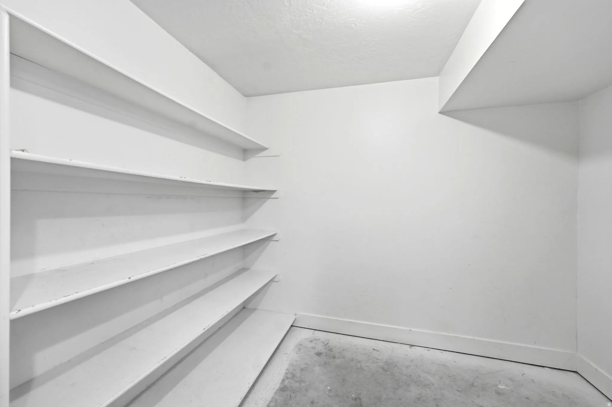 Built-in shelving with multiple storage levels, a light-colored ceiling, and concrete flooring