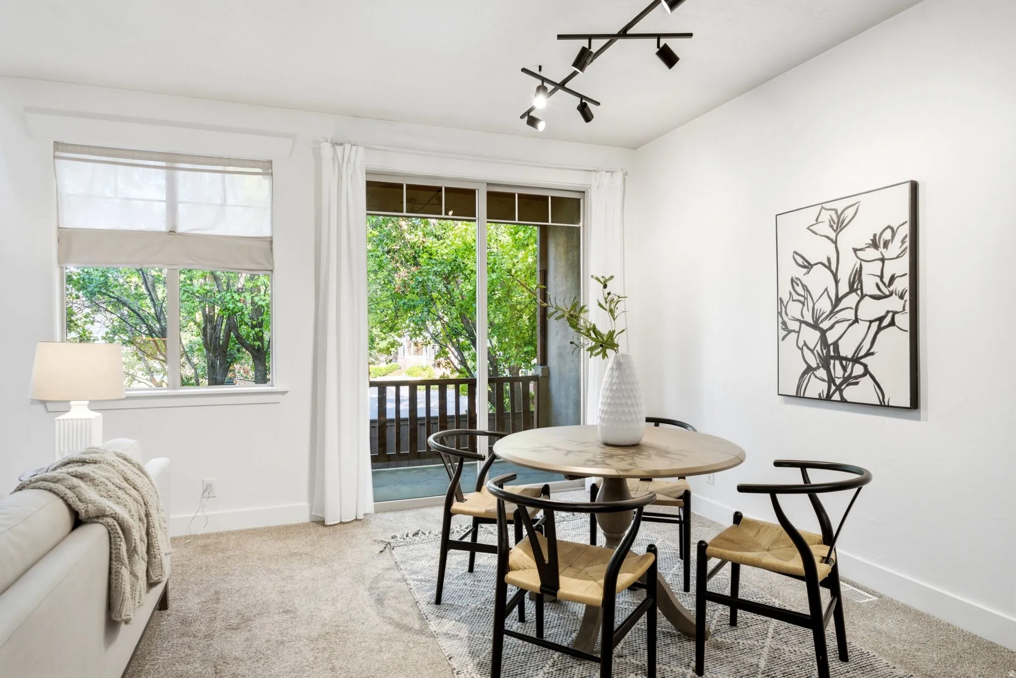 White walls with track lighting, sliding glass doors to a balcony, and a window with blinds