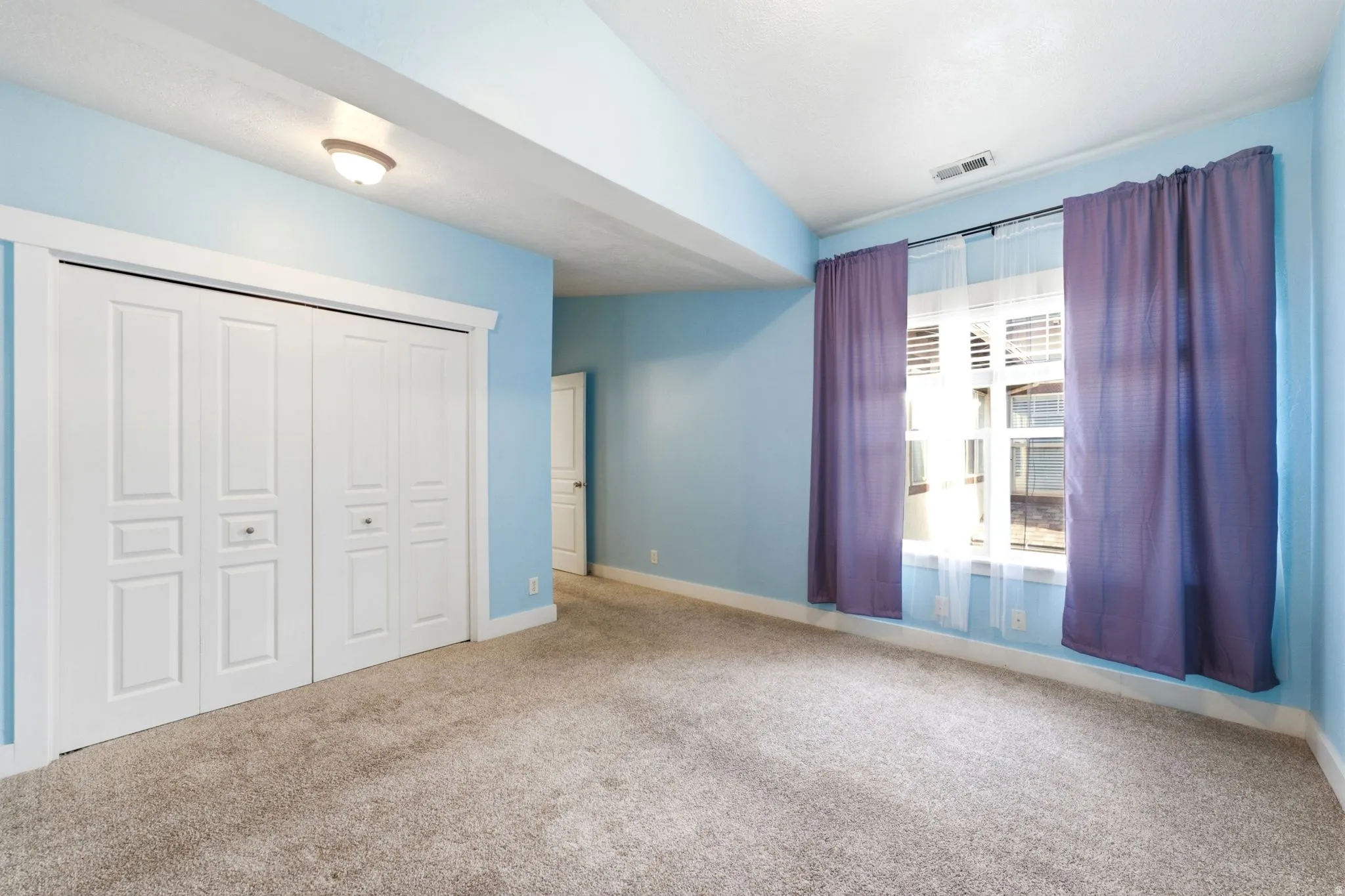 Plush carpet flooring, recessed ceiling light, double bi-fold closet doors, and window with white trim
