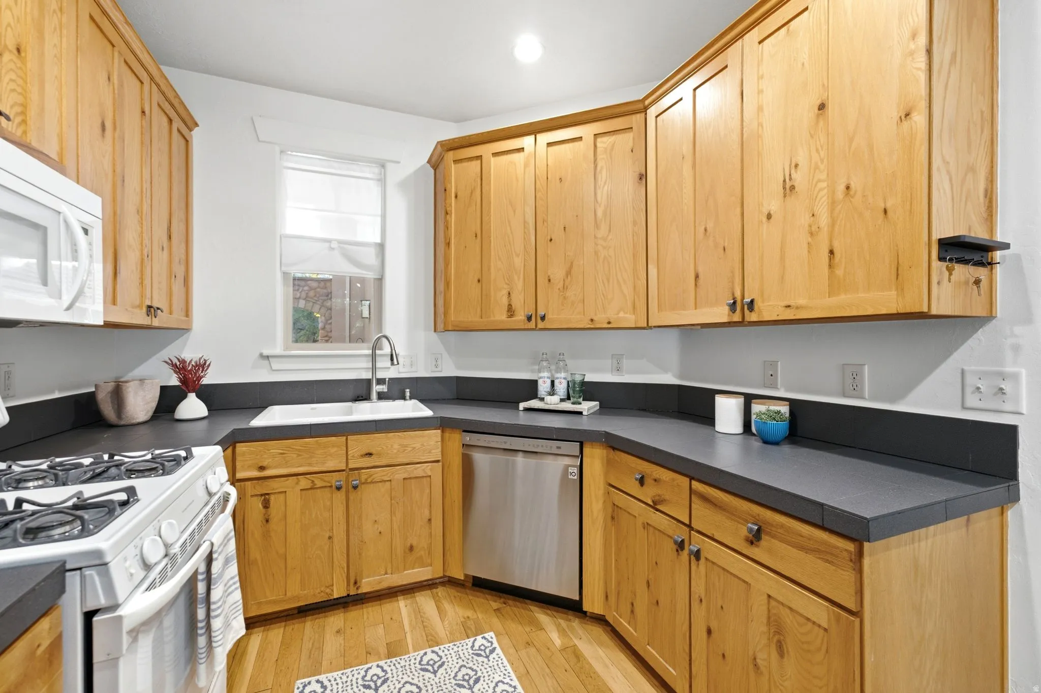 Wood-finish cabinetry paired with dark countertops, stainless steel dishwasher, and a white sink with a chrome faucet