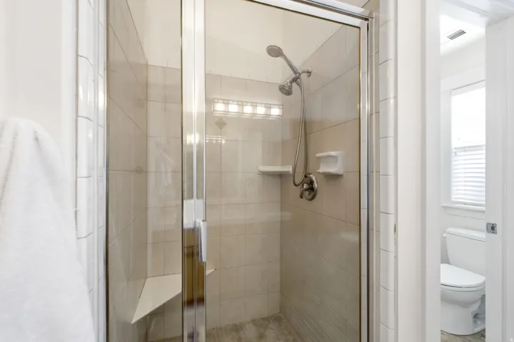 Glass-enclosed shower with a handheld showerhead, tiled walls, and a built-in bench