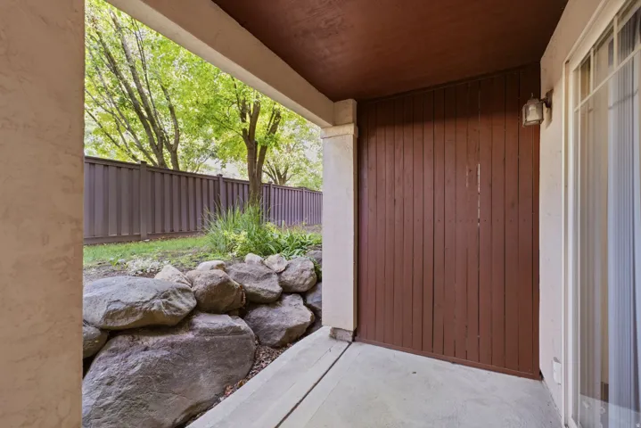 Concrete patio with a brown privacy fence, a rock garden, and mature trees beyond