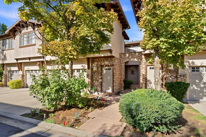 Stone facade entrance with an arched doorway, attached garages, multiple windows, and mature trees