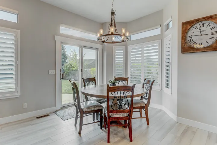 Dining area featuring light wood-finish flooring, a built-in bay window with plantation shutters, transom windows, and a glass sliding door providing outdoor access