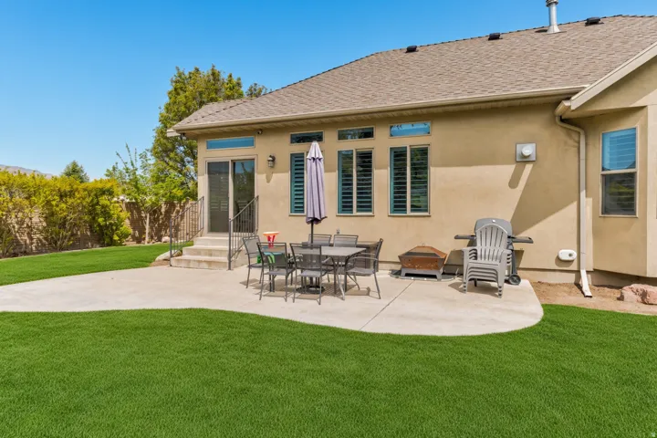 Rear exterior featuring a large concrete patio, sliding glass door entry, and multiple windows with horizontal blinds