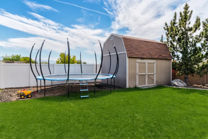 Spacious backyard featuring a storage shed with a gambrel roof and double doors, mature evergreen trees, and a white privacy fence