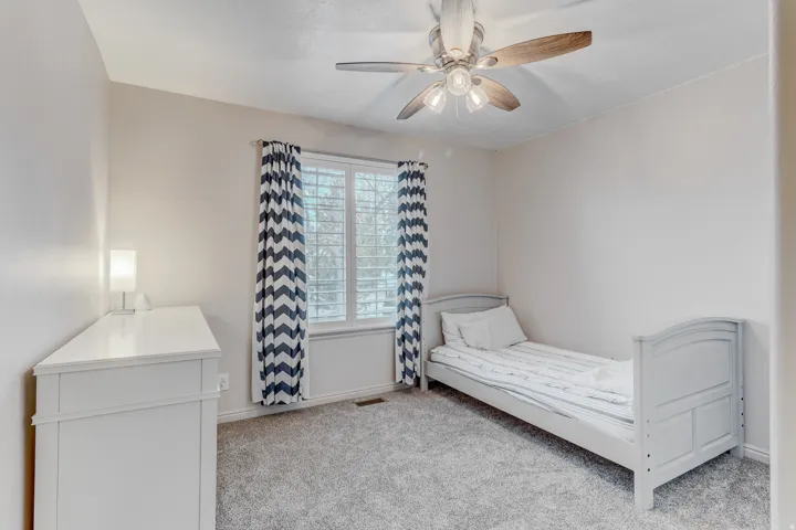 Carpeted room featuring a ceiling fan with light fixture, window with white louvered shutters, and base molding