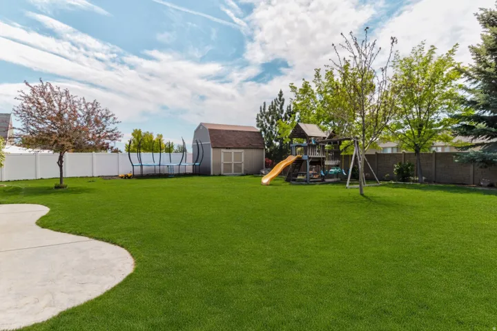 Expansive backyard featuring a manicured lawn, established trees, and a concrete patio