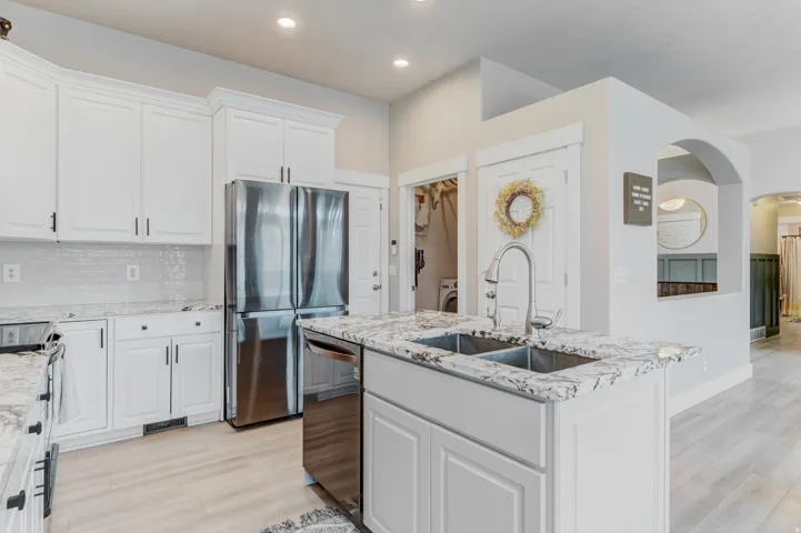 Kitchen featuring white shaker cabinetry with dark hardware, stainless steel appliances, speckled stone countertops, and a subway tile backsplash