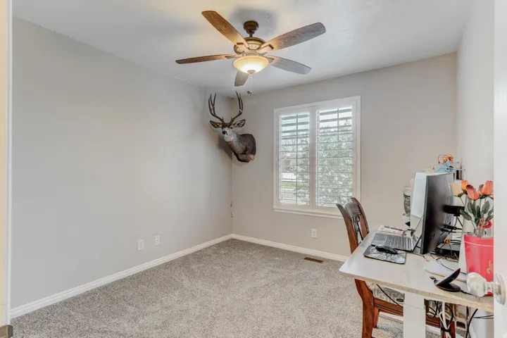Carpeted room featuring a ceiling fan with integrated lighting, a window with white plantation shutters, and light-toned walls with white baseboards