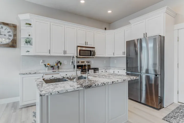 Modern kitchen featuring white cabinetry, light-toned wood-finish flooring, a stainless steel refrigerator, and a kitchen island with an undermount sink