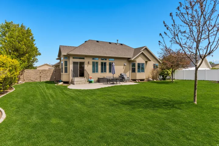 Rear exterior featuring a large concrete patio, a spacious grass lawn, and a light-colored stucco facade