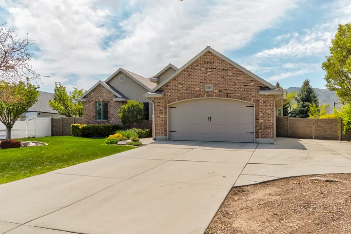 Brick-clad exterior featuring a two-car garage with an arched door, a concrete driveway, and mature landscaping