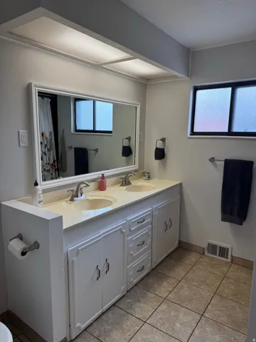 Dual vanity with integrated sinks, framed mirror, white cabinetry, and tile flooring