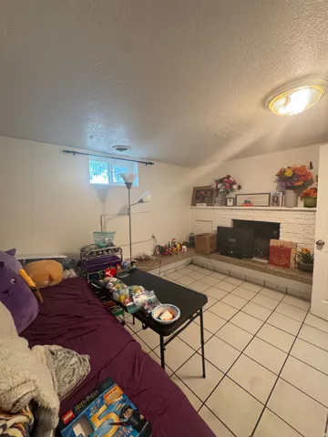 White tiled flooring, white painted walls, built-in fireplace with white brick surround, recessed ceiling lighting, and a window providing natural illumination