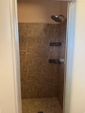 Tiled shower enclosure featuring a rainfall showerhead, and integrated shelving