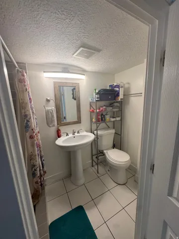White pedestal sink with a mirror above, a toilet, and light-colored floor tiles