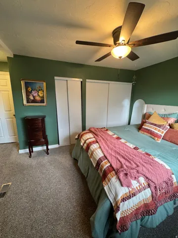 Green painted walls, ceiling fan with integrated lighting, two sliding closet doors, and light-colored carpeting