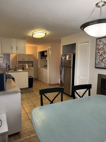 Tile flooring, white cabinetry, stainless steel refrigerator, stone-finish countertops, and flush-mount ceiling lighting