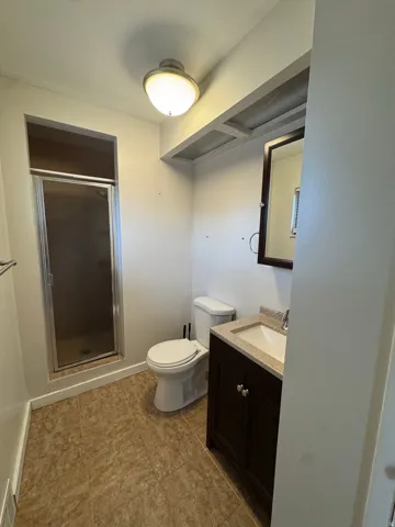 Walk-in shower with clear glass enclosure, single vanity with dark wood-finish cabinetry, countertop with integrated sink, and tile flooring
