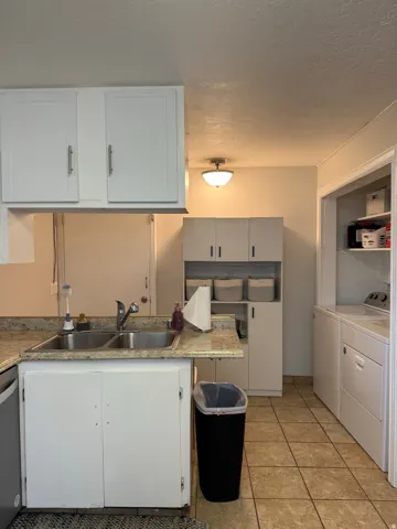 Dual basin stainless steel sink, light-toned countertop, white cabinetry with contemporary hardware, and tile flooring