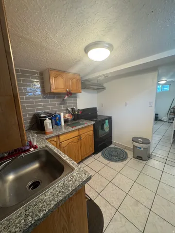 Kitchen featuring wood-finish cabinetry, stainless steel sink, speckled countertops, gray subway tile backsplash, and tile flooring