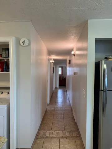 Hallway featuring tile flooring with decorative inlay, light-colored walls, and functional wall-mounted lighting