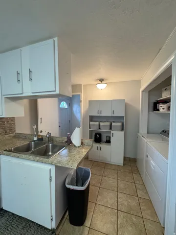 White cabinetry with brushed nickel hardware, double basin stainless steel sink, patterned tile backsplash, and light-toned countertop