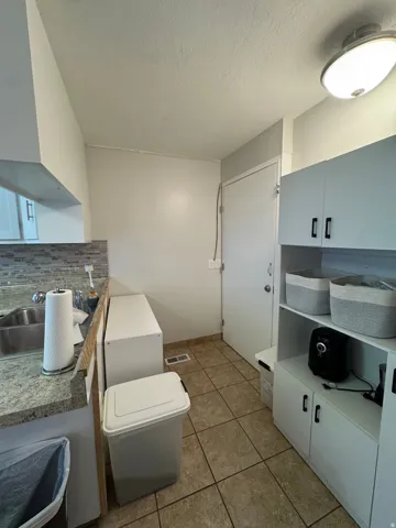 Galley-style kitchen featuring granite countertops, white cabinetry with hardware accents, tile flooring, and built-in appliances including a microwave and range
