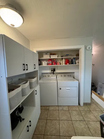 Laundry area featuring white cabinetry, built-in shelving, and neutral-toned tile flooring