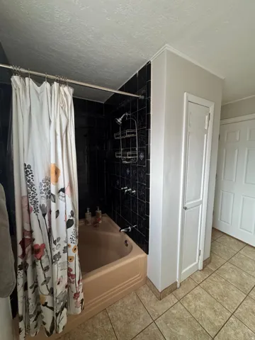 Built-in bathtub with black tiled surround, chrome fixtures, and neutral-toned floor tile
