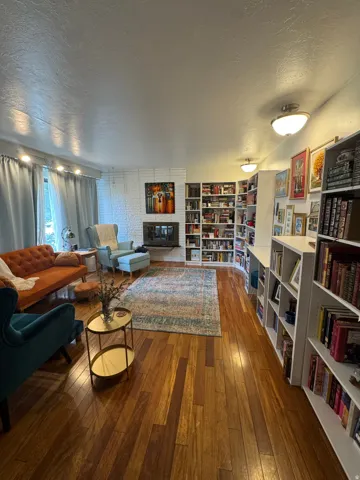 Wood-finish flooring, white brick fireplace, multiple flush-mount light fixtures, track lighting, and extensive built-in shelving